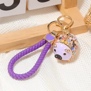 Detail von lila geflochtenem Lederband und goldenem Schweineanhänger mit bunten Kristallen