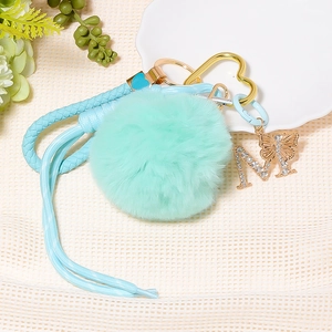 Detail of mint green pompom keychain with gold letter M charm and woven strap