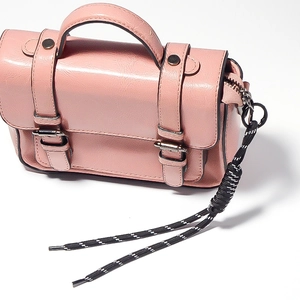 Detail of pink PU leather handbag with metal buckle and black and white braided rope charm