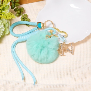 Detail of light blue faux fur pompom and rhinestone letter N charm on woven keychain