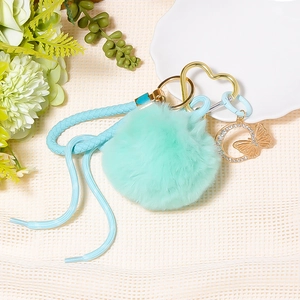 Detail of mint green pompom keychain with braided rope and golden heart clasp
