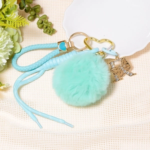 Detail of light blue fluffy pompom keychain with a gold rhinestone butterfly letter R