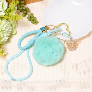 Close-up of a mint green fluffy pom-pom keychain with heart clip and rhinestone butterfly