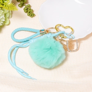 Detail of mint green faux fur pompom keychain with blue braided strap and crystal letter U