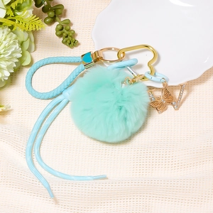 Detail of mint green pompom keychain with gold butterfly and crystal letter charm