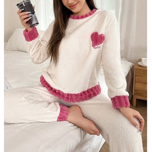 Detail of coral fleece pajamas with pink heart embroidery and ruffled edges on cream fabric