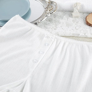 Detail of white pointelle knit pajamas with lace trim, bow, and decorative buttons