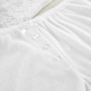 Close-up of white knitted pajama detail with lace trim, satin bow and clear buttons