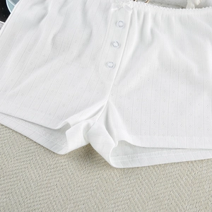 Close-up of white knitted sleep shorts with lace trim, bow, and button detailing