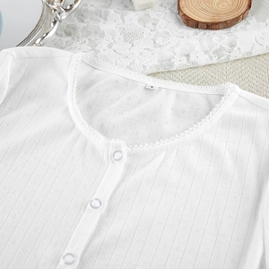 Macro shot of white knitted pajama top with lace trim, buttons and diamond texture