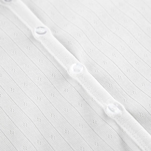 Close-up of white knitted jacquard fabric with delicate hollow patterns and clear buttons
