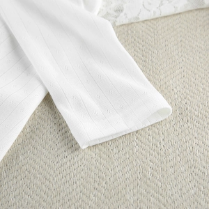 Macro view of white pointelle knit sleeve with delicate ribbed texture and lace details