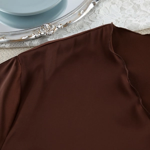 Detailed macro shot of dark brown satin fabric texture and premium hemline craftsmanship