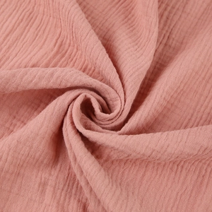 Macro detail of breathable coral pink double gauze cotton fabric with natural crinkled texture