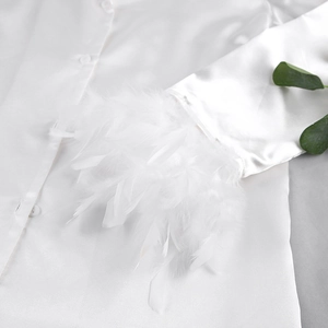 Détail de la manche de pyjama en satin blanc avec poignets en plumes et texture de soie