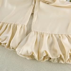 Detail of light champagne satin pajamas featuring elegant wide ruffled hem and silky texture