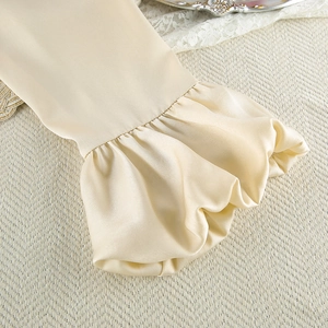 Close-up of elegant ivory satin pajamas featuring silk ruffles and smooth fabric texture