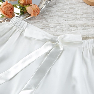 Detail of white satin sleepwear shorts featuring elastic waistband and delicate bow tie