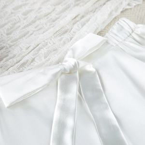 Detail of white satin shorts featuring an elastic waistband and a silky bow tie detail