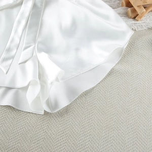 Close-up of white satin pajama shorts with ribbon ties on a textured beige rug