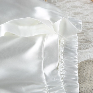 Detailed macro shot of pearl white satin pajama shorts with elastic waistband and pleats