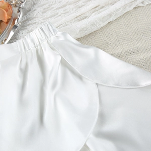 Detailed macro view of white satin lounge shorts with pleated waistband and petal hem design