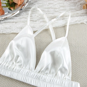 Close-up of white satin camisole with V-neckline and elastic hem on a woven texture mat