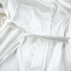Close-up of white satin sleeprobe texture with matching waist tie on soft beige carpet