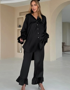 Detail van zwarte satijnen pyjamaset met overhemd en broek met ruches aan de zoom