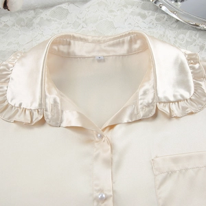 Detail van champagne satijnen pyjamastop met ruffelkraag en knopen van parelmoer