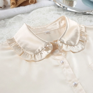 Detail van satijnen pyjamabovenstuk met ruffelkraag en elegante parelknoppen
