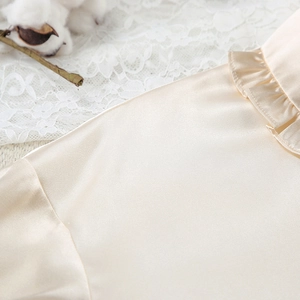 Detail van beige satijnen pyjama-top met ruches bij de hals en zijdeachtige textuur