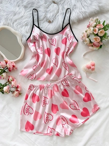 Close-up of pink satin pajama set with heart patterns on a cozy white bed background
