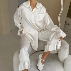 Elegante witte satijnen pyjamaset met ruches aan kraag en lange broek in huiselijke sfeer