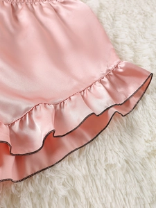 Detail of pink satin pajama shorts with ruffled hem and black contrast piping