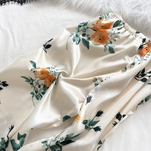 Silk-like pajama pants with orange rose floral print and elastic waist on plush background