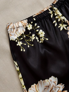 Detail of black satin pajama pants with elastic waistband and large floral print
