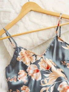 Detail of satin floral camisole top featuring V-neck and thin straps on wood hanger