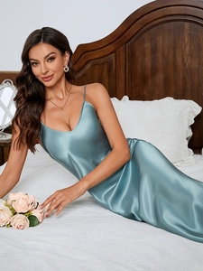 Detail of teal satin slip dress with V-neckline and spaghetti straps on a soft bed