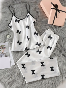 Ensemble pyjama caraco en satin blanc à motifs de nœuds noirs posé sur tapis en peluche