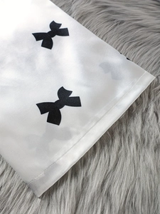 Détail du tissu satiné blanc avec imprimé nœud noir et coutures de haute qualité
