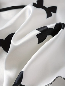 Détail de tissu en satin blanc avec imprimé nœud noir et bordure cousue