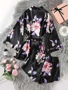 Flat lay of black floral satin robe set with shorts on a plush grey rug with pink gift box