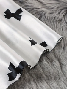 Détail du tissu en satin blanc avec imprimé nœud noir et finition de surjet fine