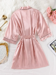 Détail de la texture d'un peignoir en satin rose avec liseré foncé sur le col et les manches