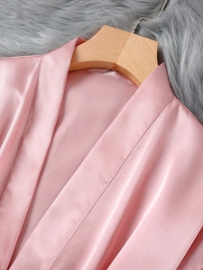 Gros plan détaillé d'un peignoir en satin rose avec col en V sur un cintre en bois et fond peluche