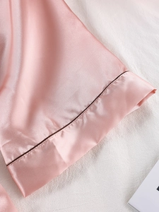 Détail de la manche d'un peignoir en satin rose avec liseré marron et tissu soyeux brillant