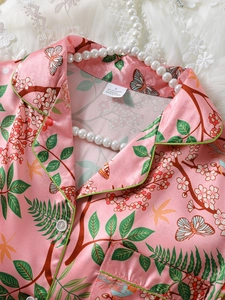Detailed view of pink satin pajama shirt with butterfly prints and green piping trim