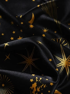 Detail der Seidenpyjamas mit goldenen Sonnen- und Mondmotiven auf schwarzem Satin