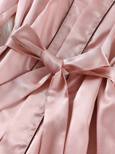 Détail d'un peignoir en satin rose avec nœud à la taille et liserés contrastants